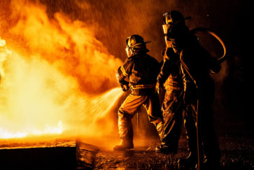 Two firefighters fighting a fire with a hose and water